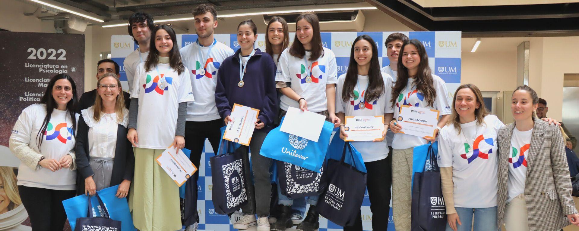 Grupo de preuniversitarios posan con premios, junto a organizadores del Challenge UM. Visten camisetas con formas de colores que identifican a la campaña 2022 de la UM.